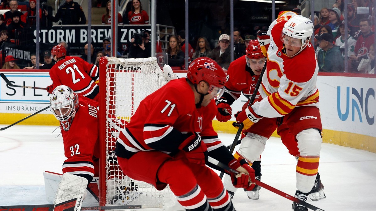Hráč Calgary Flames Dryden Hunt (15) bojuje o puk medzi hráčmi Caroliny Hurricanes Taylorom Hallom (71) a Joelom Nystromom (64).