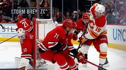 Hráč Calgary Flames Dryden Hunt (15) bojuje o puk medzi hráčmi Caroliny Hurricanes Taylorom Hallom (71) a Joelom Nystromom (64).
