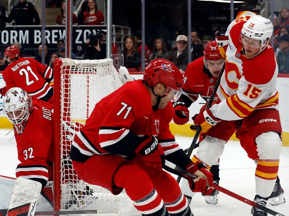 Hráč Calgary Flames Dryden Hunt (15) bojuje o puk medzi hráčmi Caroliny Hurricanes Taylorom Hallom (71) a Joelom Nystromom (64).
