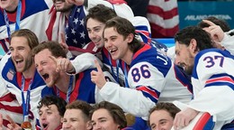 Jack Hughes (uprostred) s vybitým zubom oslavuje zisk zlatej medaily na ZOH 2026. 