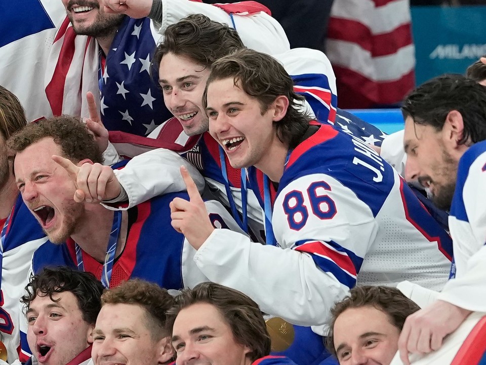 Jack Hughes (uprostred) s vybitým zubom oslavuje zisk zlatej medaily na ZOH 2026.