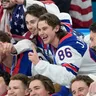 Jack Hughes (uprostred) s vybitým zubom oslavuje zisk zlatej medaily na ZOH 2026.