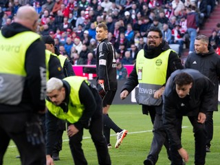 Stevardi zbierajú predmety z trávnika a v pozadí brankár Manuel Neuer z Bayernu Mníchov počas zápasu 20. kola nemeckej Bundesligy proti Borussii Mönchengladbach. 