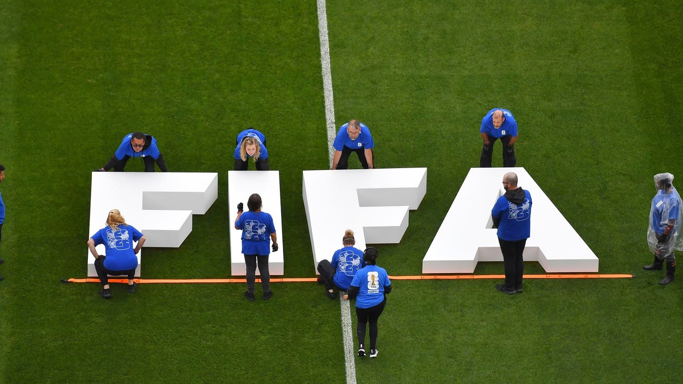 Na snímke pracovníci umiestňujú na trávnik nápis Medzinárodnej futbalovej federácie (FIFA).