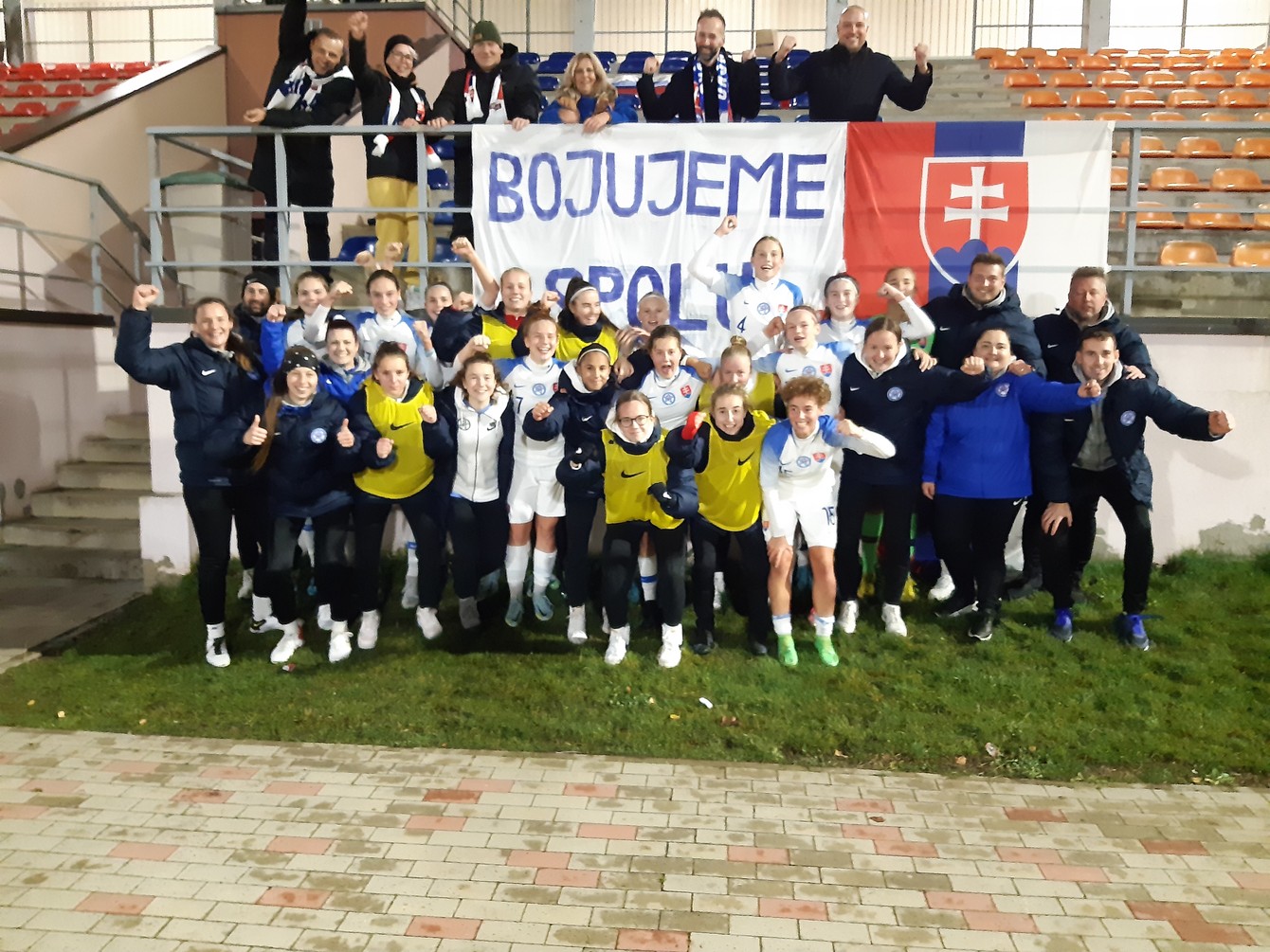 Postupová radosť tímu WU17 a na tribúne podpora zo slovenskej ambasády v Rige.
