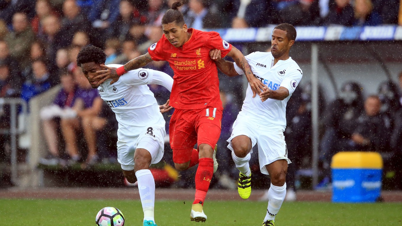 Roberto Firmino (v strede) sa pokúša preniknúť cez dvoch hráčov Swansea City. V zápase strelil prvý gól Liverpoolu.