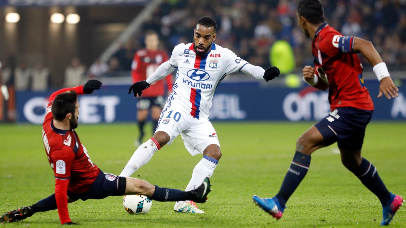 Alexandre Lacazette (v strede) z Lyonu sa pokúša presadiť cez dvoch brániacich futbalistov súpera.