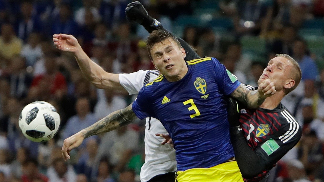 Švédsky brankár Robin Olsen boxuje loptu v súboji s Nemcom Julianom Draxlerom, ktorého bráni Victor Lindelöf.