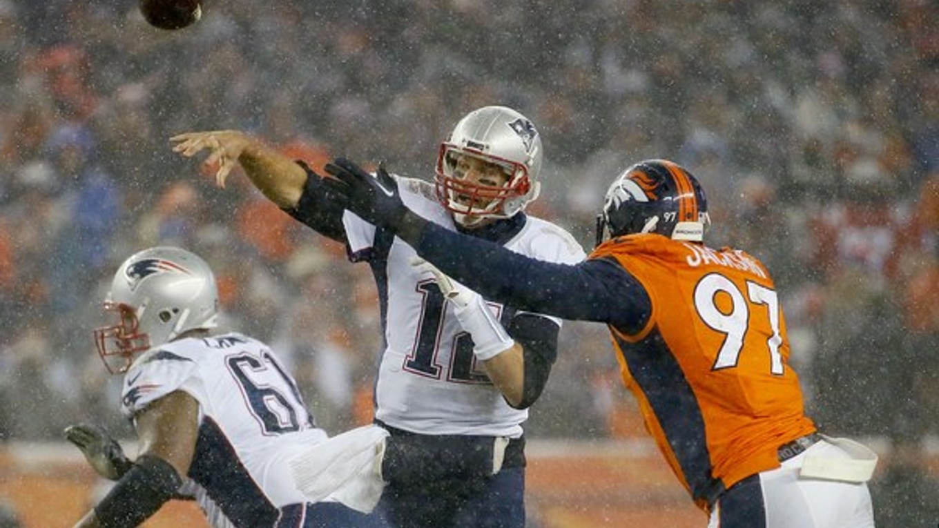 Na snímke zo zápasu medzi tímami New England Patriots a Denver Broncos hádže loptu quarterback Patriots Tom Brady (v strede). Oba tímy už štvrtý rok za sebou skončili na prvých dvoch priečkach v konferencii American Football.