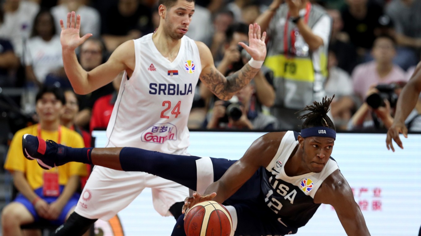 Myles Turner padá s loptou a vľavo hráč Srbska Stefan Jovič v zápase skupiny o 5. - 8. miesto na MS v basketbale mužov Srbsko - USA.