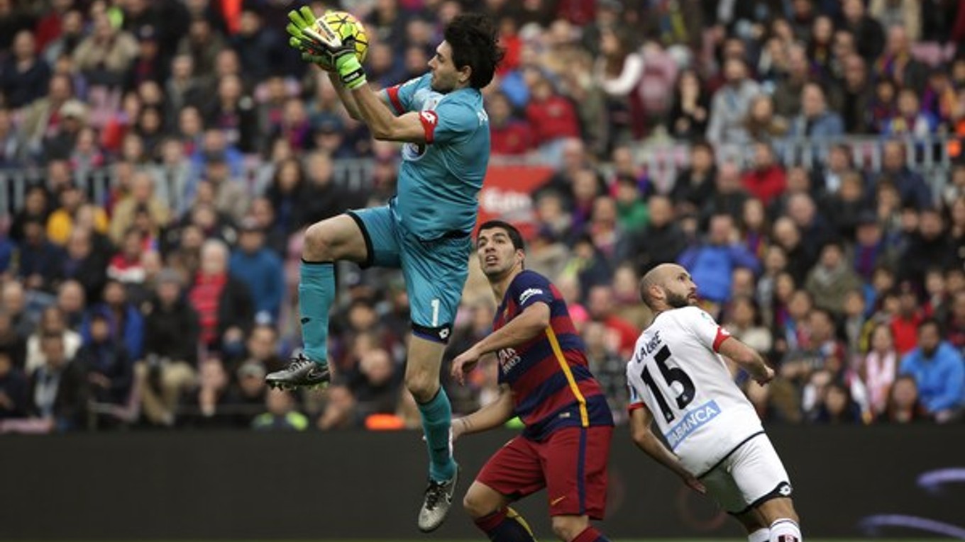 Brankár Deportiva La Coruňa Dario Lux chytá loptu vo výskoku pred Luisom Suárezom.