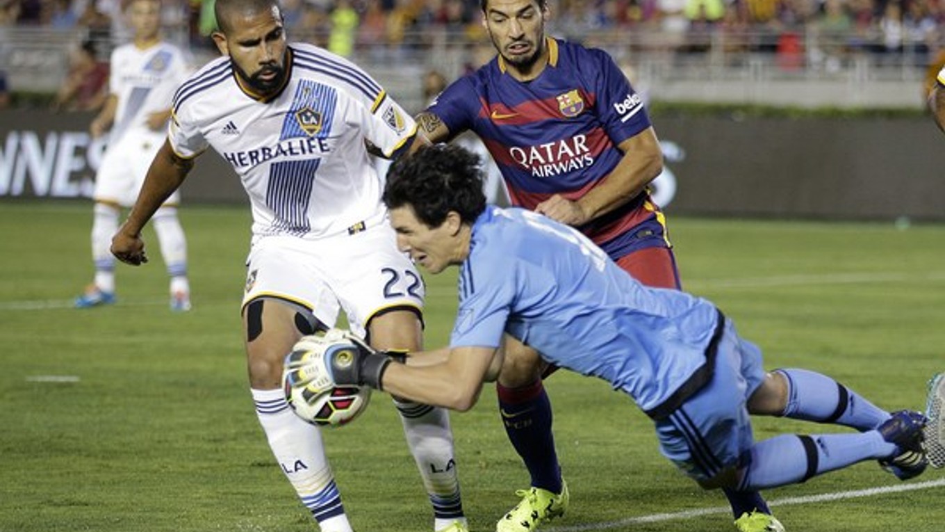 Brankár Los Angeles Galaxy Brian Rowe chytá loptu pred dobiedzajúcim Luisom Suárezom z Barcelony. Situáciu kontroluje jeho spoluhráč Leonardo (s číslom 22).