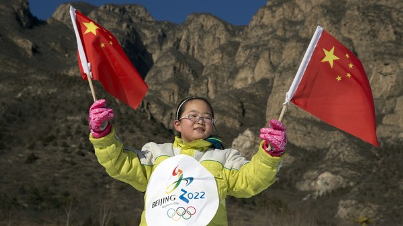Čínske dievčatko máva s národnými vlajkami a na bunde má logo oficiálnej kandidatúry Pekingu na organizáciu ZOH v roku 2022.