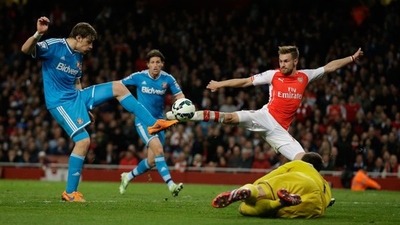 Futbalista Arsenalu Aaron Ramsey (v červenom drese) sa snaží zakončiť pred ležiacim brankárom Sunderlandu Costelom Pantilimonom. Bráni ho Sebastian Coates (vľavo).