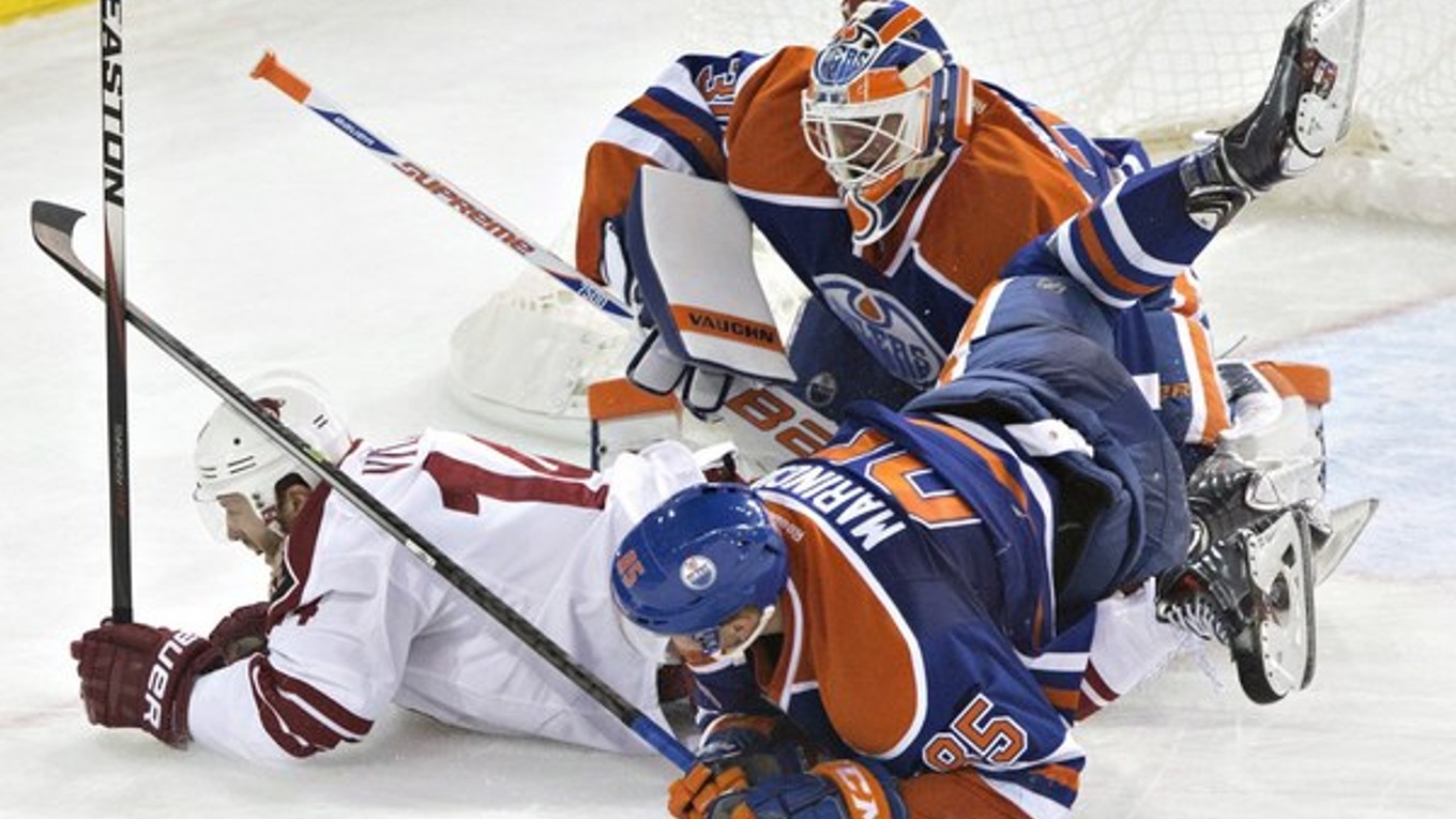 Hráč Arizony Coyotes Joe Vitale (14) a Slovák Martin Marinčin z Edmontonu Oilers (85) padajú na brankára Edmontonu Bena Scrivensa (30) v tretej tretine prípravného zápasu NHL v Edmontone 1. októbra.