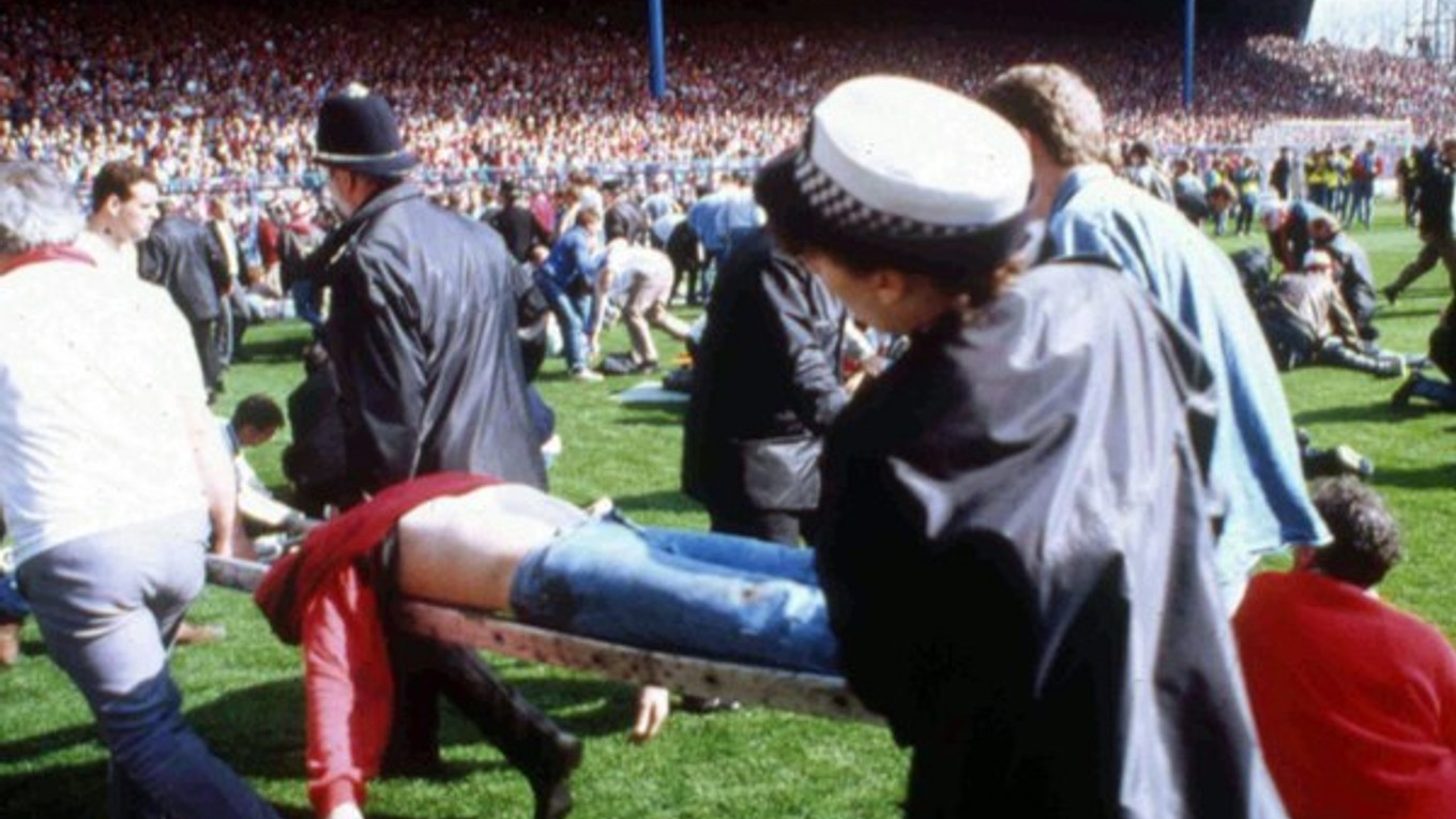 Na archívnej snímke z 15. apríla 1989 futbaloví fanúšikovia a policajti pomáhajú zraneným fanúšikom na ihrisku štadióna Hillsborough v Sheffielde počas obrovskej tragédie, pri ktorej zahynulo 96 fanúšikov Liverpoolu.