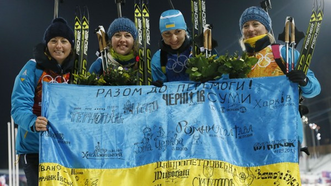 Ukrajinský tím pózuje so zástavou po víťazstve v biatlonovej štafete.