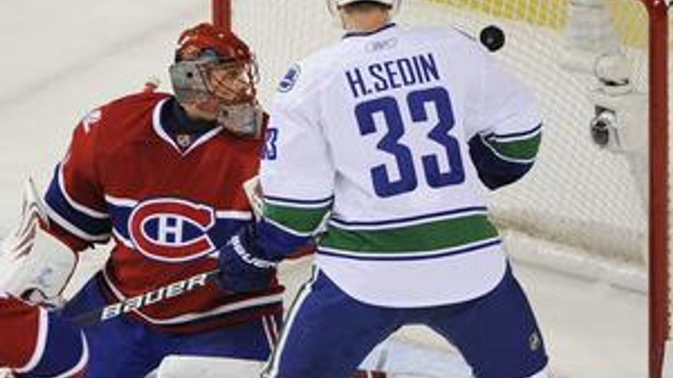 Slovenský brankár Montrealu Canadiens Jaroslav Halák sa pozerá na puk smerujúci do jeho bránky z hokejky Mikaela Samuelssona z Vancouvru. Prizerá sa Henrik Sedin z Canucks.
