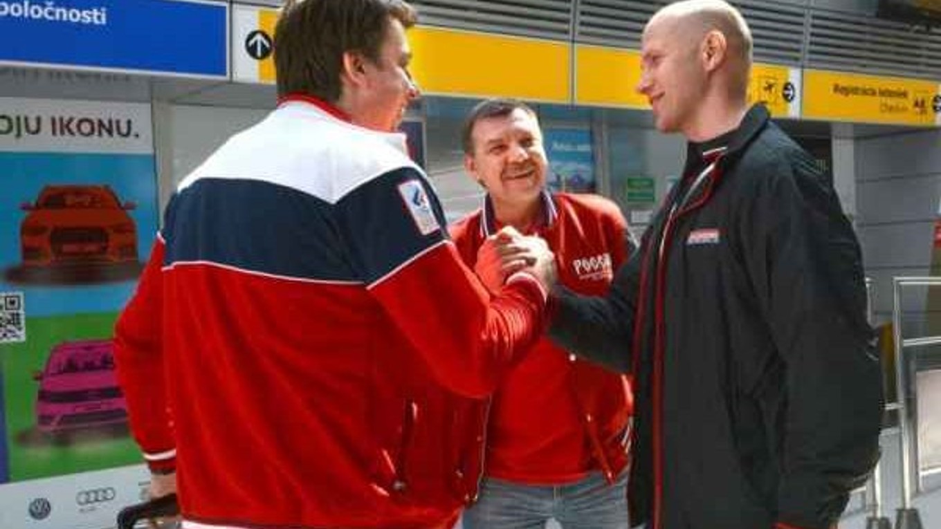 Tréner ruskej reprezentácie O. Znarok (v strede) v letiskovej hale s úsmevom na tvári.