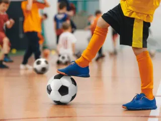 Football futsal training for children. Soccer training drill. Indoor soccer young player with a soccer ball in a sports hall. Player in yellow uniform. Sport background