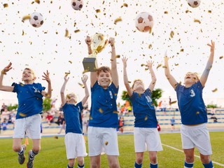 Happy Boys Celebrating Soccer Championship. Youth Football Winning Team Jumping and Rising Golden Cup on Trophy Ceremony After the Final Tournament Game. Football Stadium and Fans in the Background