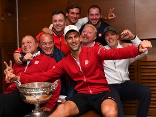 Šťastný Djokovič pózuje v šatni s víťazným pohárom spolu so svojím tímom.
