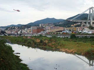 Na snímke hasičská helikoptéra prelietava nad troskami časti zrúteného diaľničného Morandiho mosta.