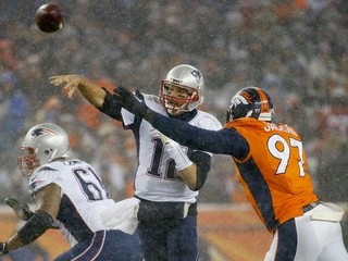 Na snímke zo zápasu medzi tímami New England Patriots a Denver Broncos hádže loptu quarterback Patriots Tom Brady (v strede). Oba tímy už štvrtý rok za sebou skončili na prvých dvoch priečkach v konferencii American Football.