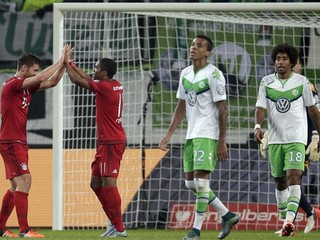 Futbalisti Bayernu Xabi Alonso (vľavo) a Douglas Costa sa tešia z gólu do siete Wolfsburgu, hráči súpera smútia.