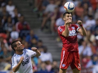 Octavio Rivero z tímu Vancouver Whitecaps sa prizerá, ako hlavičkuje loptu jeho súper Matt Hedges z Dallasu.