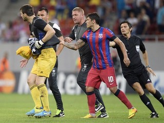 Slovenský brankár Legie Dušan Kuciak (vľavo) ukazuje rozhodcovi predmet, ktorý hodil po ňom fanúšik, zastaviť sa ho snaží hráč Bukurešti Cristian Tanase (uprostred).