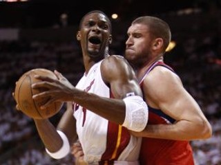 Hviezda Miami Heat Chris Bosh (v bielom) bránený Spencerom Hawesom (Philadelphia 76ers)
