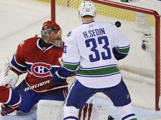 Slovenský brankár Montrealu Canadiens Jaroslav Halák sa pozerá na puk smerujúci do jeho bránky z hokejky Mikaela Samuelssona z Vancouvru. Prizerá sa Henrik Sedin z Canucks.