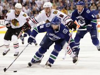 Pavol Demitra z Vancouveru (uprostred) uniká s pukom pred Mattom Walkerom z Chicago Blackhawks.