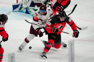 Latvia's Kristaps Roberts Zile (77) battles for the puck against Canada's Cody Glass (8) during their semifinal match at the Ice Hockey World Championship in Tampere, Finland, Saturday, May 27, 2023. (AP Photo/Pavel Golovkin)