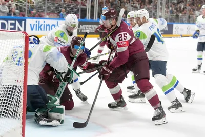 Andris Dzerins, right, and Kristaps Zile, centre of Latvia, fight for a puck with goalie Gasper Kroselj of Slovenia during the group B match between Latvia and Slovenia at the ice hockey world championship in Riga, Latvia, Friday, May 19, 2023. (AP Photo/Roman Koksarov)