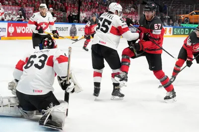 Goalie Leonardo Genoni, left, and Romain Loeffel, centre, of Switzerland fight for a puck with Lawson Crouse of Canada during the group B match between Switzerland and Canada at the ice hockey world championship in Riga, Latvia, Saturday, May 20, 2023. (AP Photo/Roman Koksarov)