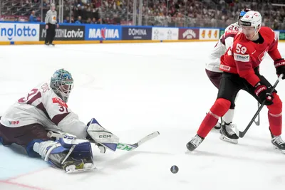 Goalie Arturs Silovs of Latvia, left, fights for a puck with Dario Simion of Switzerland during the group B match between Latvia and Switzerland at the ice hockey world championship in Riga, Latvia, Tuesday, May 23, 2023. (AP Photo/Roman Koksarov)