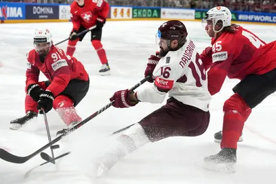 Kaspars Daugavins of Latvia, centre, fights for a puck with Michael Foro, right, and Jonas Siegenthaler, left, of Switzerland during the group B match between Latvia and Switzerland at the ice hockey world championship in Riga, Latvia, Tuesday, May 23, 2023. (AP Photo/Roman Koksarov)
