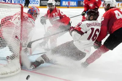 Kaspars Daugavins of Latvia, centre, fights for a puck with Michael Foro, right, Jonas Siegenthaler, left, and goalie Joren Pottelberghe of Switzerland during the group B match between Latvia and Switzerland at the ice hockey world championship in Riga, Latvia, Tuesday, May 23, 2023. (AP Photo/Roman Koksarov)
