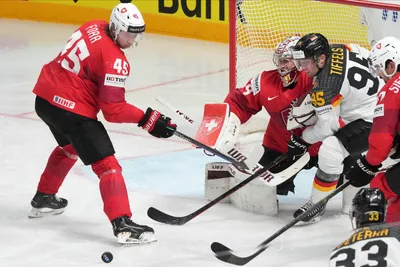 Frederik Tiffels of Germany, second right, fights for a puck with goalie Robert Mayer, centre, and Michael Foro of Switzerland during the quarter final match between Germany and Switzerland at the ice hockey world championship in Riga, Latvia, Thursday, May 25, 2023. (AP Photo/Roman Koksarov)