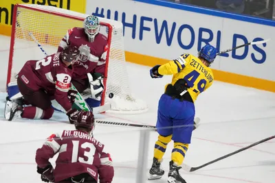Goalie Arturs Silovs of Latvia, left, fights for a puck with Fabian Zetterlund of Sweden during the quarter final match between Latvia and Sweden at the ice hockey world championship in Riga, Latvia, Thursday, May 25, 2023. (AP Photo/Roman Koksarov)