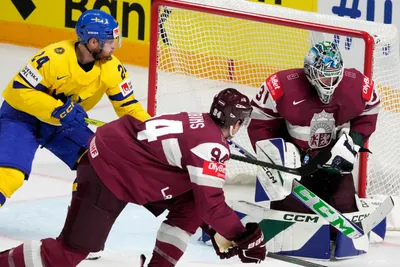 Goalie Arturs Silovs of Latvia, right, fights for a puck with Oscar Lindberg of Sweden during the quarter final match between Latvia and Sweden at the ice hockey world championship in Riga, Latvia, Thursday, May 25, 2023. (AP Photo/Roman Koksarov)