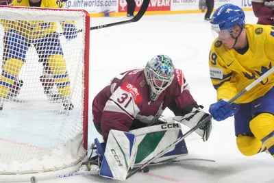 Goalie Arturs Silovs of Latvia, center, fights for a puck with Fabian Zetterlund of Sweden during the quarter final match between Latvia and Sweden at the ice hockey world championship in Riga, Latvia, Thursday, May 25, 2023. (AP Photo/Roman Koksarov)