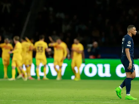 Kylian Mbappé kráča na ihrisku, zatiaľ čo Raphinha z Barcelony oslavuje so spoluhráčmi úvodný gól.