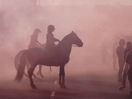 Policajti na koňoch hliadkujú, zatiaľčo fanúšikovia zapaľujú svetlice.