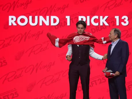 Carter Bear (vľavo) si oblieka dres vedľa komisára NHL Garyho Bettmana po tom, ako si ho v piatkovom drafte NHL 27. júna 2025 v Los Angeles vybral tím Detroit Red Wings.
