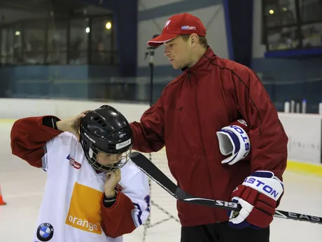 Slovenský hokejista Marián Gáborík upravuje výstroj mladému hokejistovi počas tréningu so žiakmi hokejovej školy.