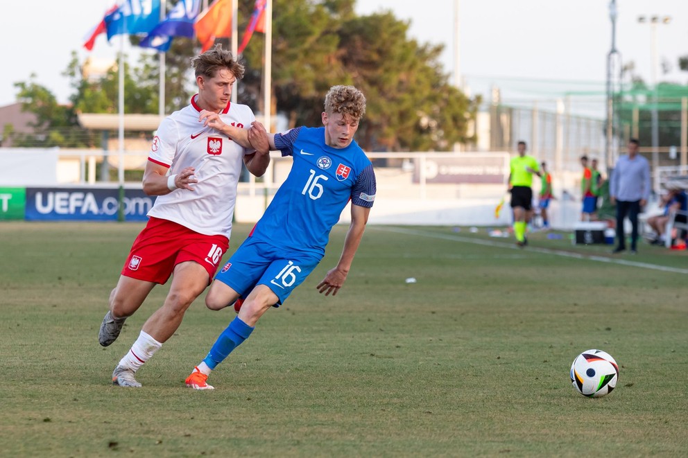 V 23-člennej nominácii je aj 11 futbalistov, ktorí sa v máji predstavili na ME do 17 rokov na Cypre. Medzi nimi aj Samuel Kováčik (na snímke v modrom v súboji s Baroszom Krieglerom v zápase proti Poľsku 17 na ME do 17 rokov, 27.5.2024)