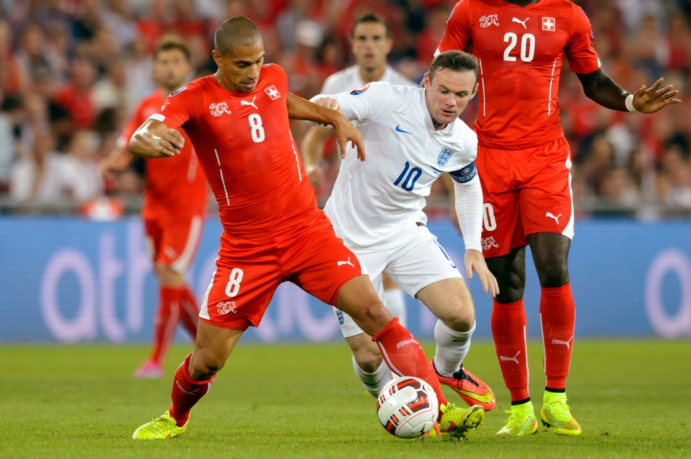 Gökhan Inler (s číslom 8) je aj bývalým kapitánom Švajčiarska. Na snímke bojuje o loptu s hráčom Anglicka Waynom Rooneym.